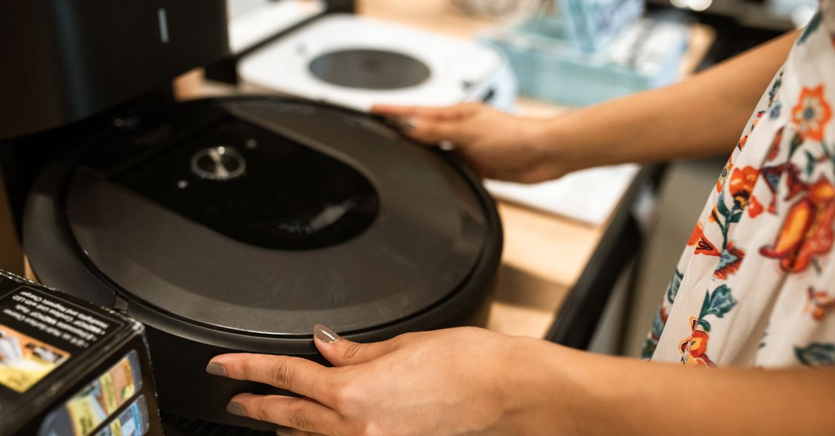 A customer examines a sleek robotic vacuum cleaner in a modern store.